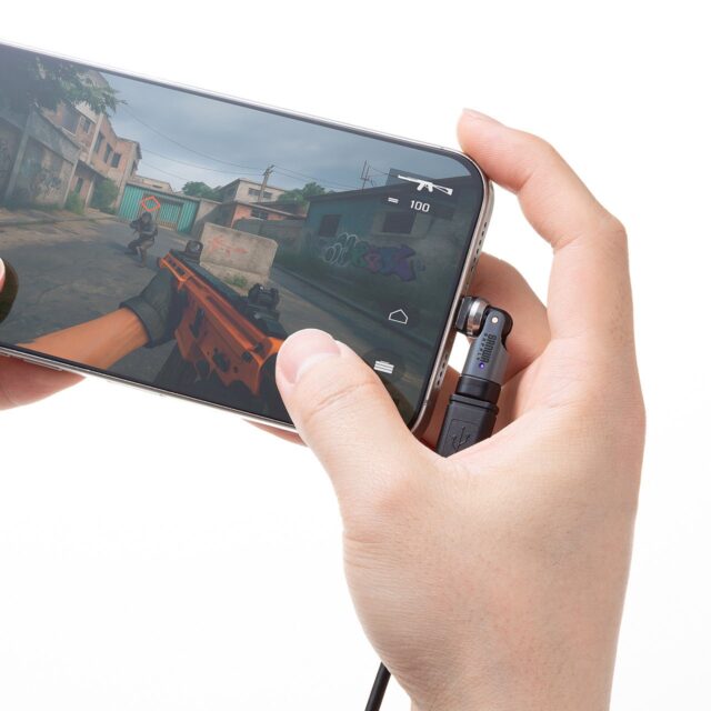 記事画像2: スマホでシューティングゲームをプレイ。横向きに持ち、充電アダプタが接続されている。