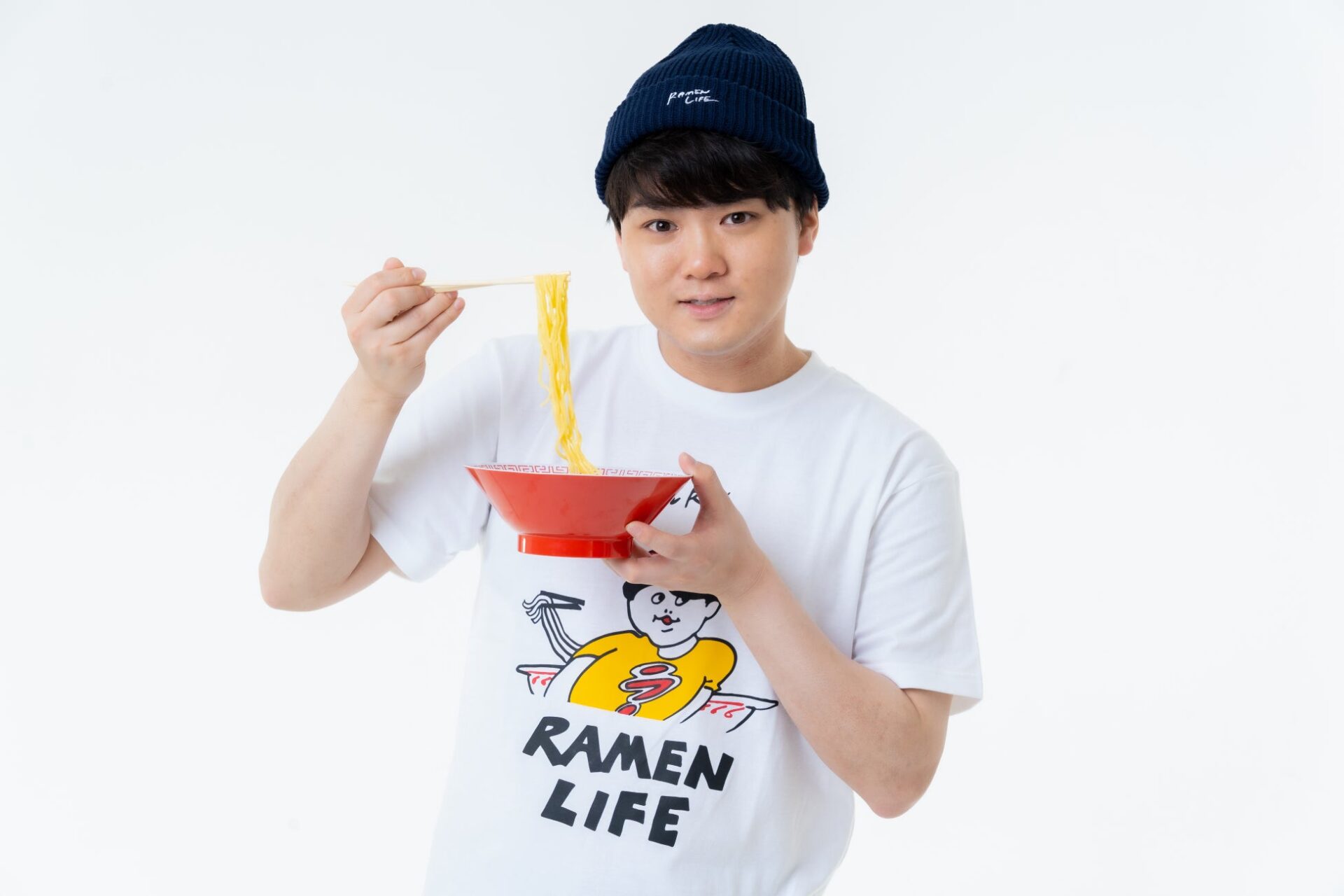 記事画像12: 男性がラーメンと箸を持ち、笑顔でカメラを見ている