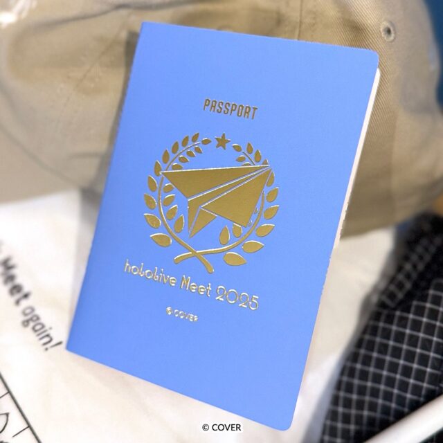 記事画像3: 水色のパスポート風ノートに「PASSPORT」と「hololive Meet 2025」の文字、金の紙飛行機と月桂樹のモチーフがデザインされている。