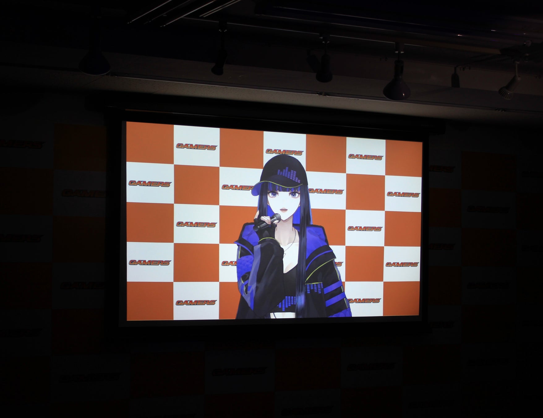 記事画像2: VTuberがマイクに向かって話している様子が映し出されたスクリーン