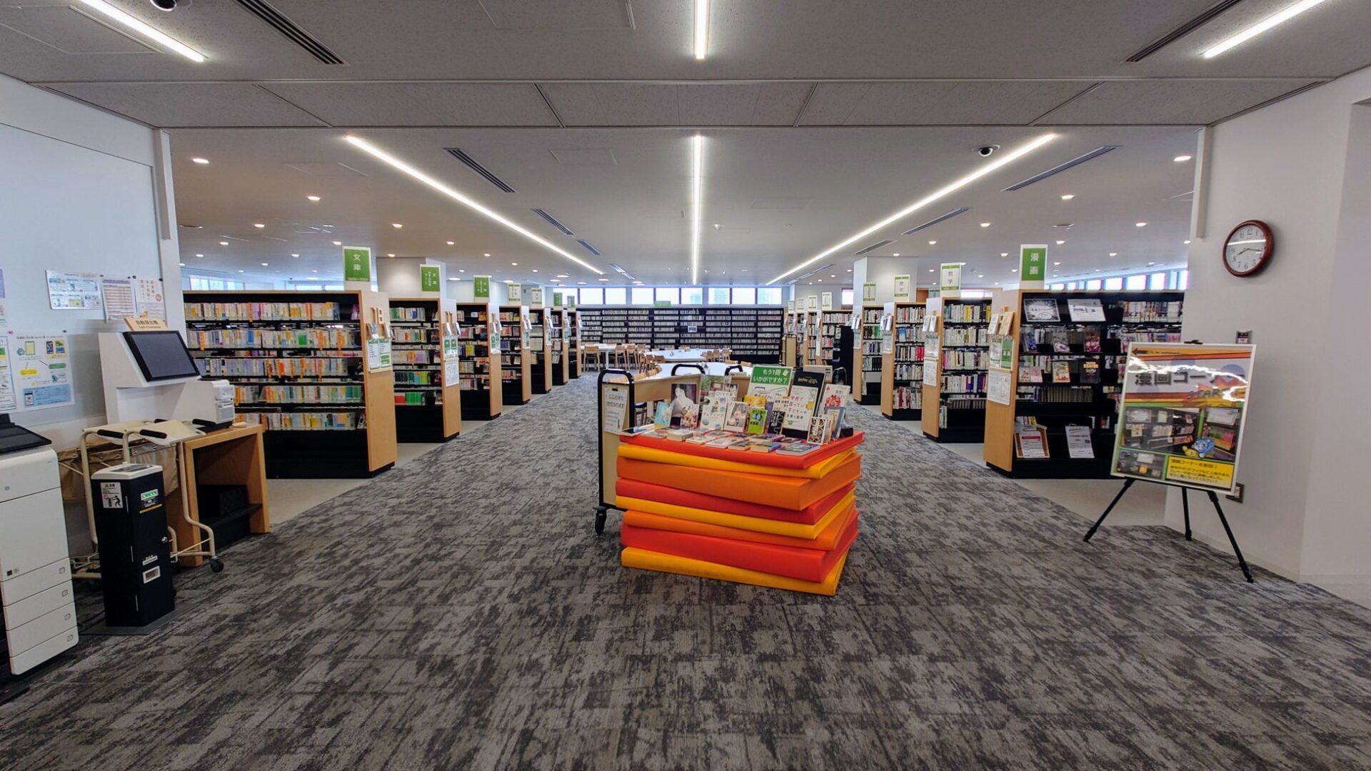 記事画像2: 明るくモダンな図書館の様子。書籍が並んだ書棚と、手前には展示用の台車。