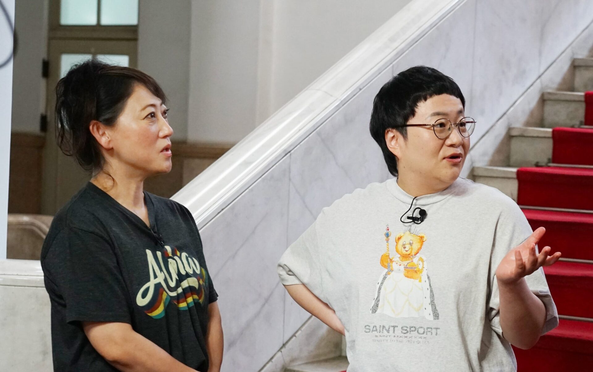 記事画像4: 女性と男性が階段を背景に話している。