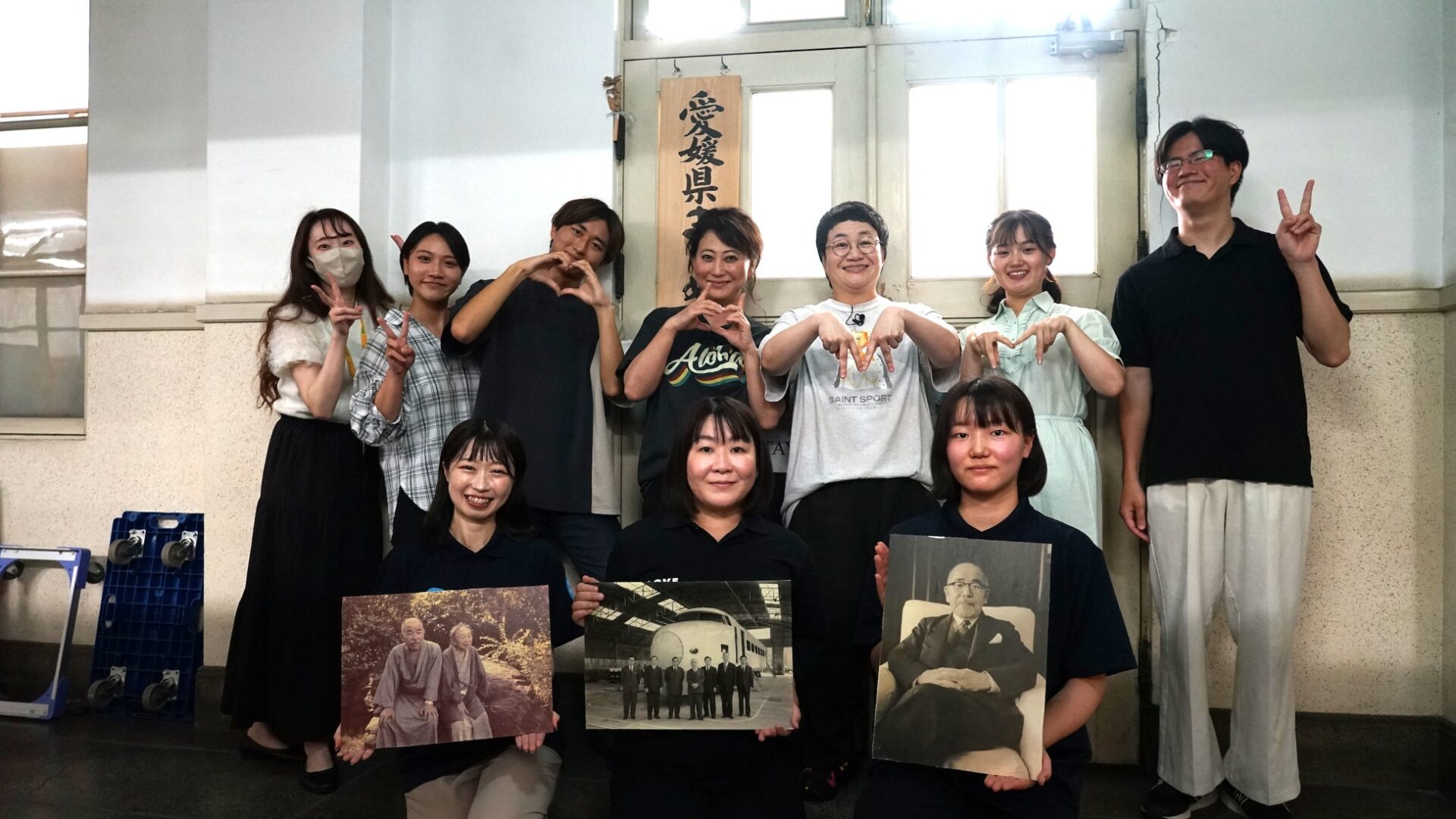 記事画像6: 8人の人々がポーズをとって写真を撮っている。3人が写真を手に持っている。
