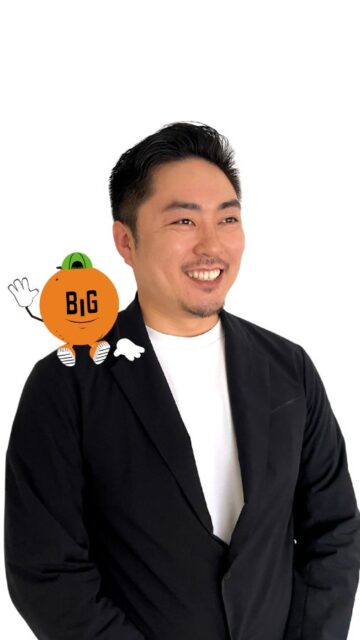 記事画像6: 男性が黒いジャケットを着て、肩にオレンジ色のキャラクターが乗っている。