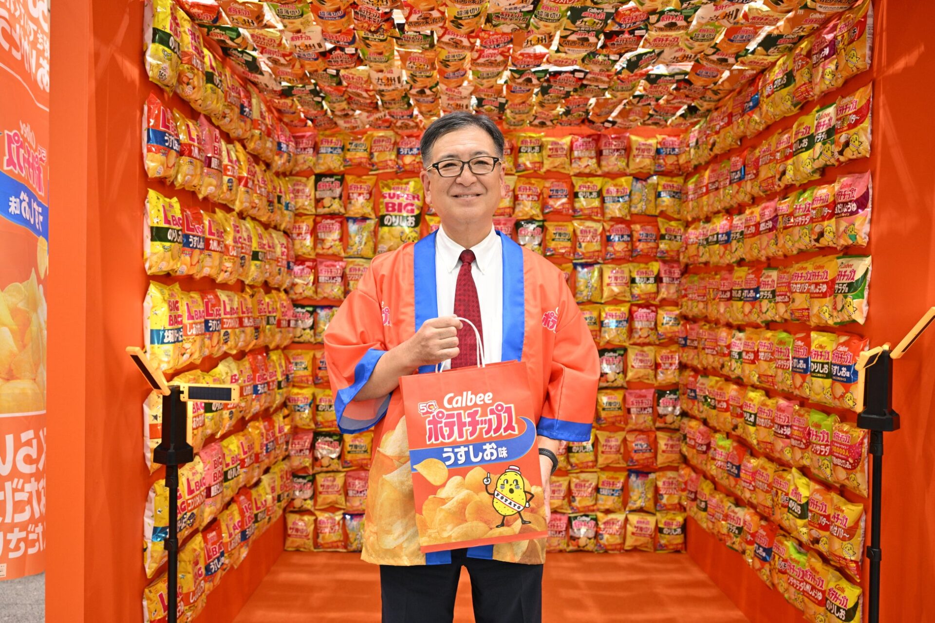 記事画像6: 男性がカルビーポテトチップスを手に、ポテトチップスで埋め尽くされた部屋に立っている。