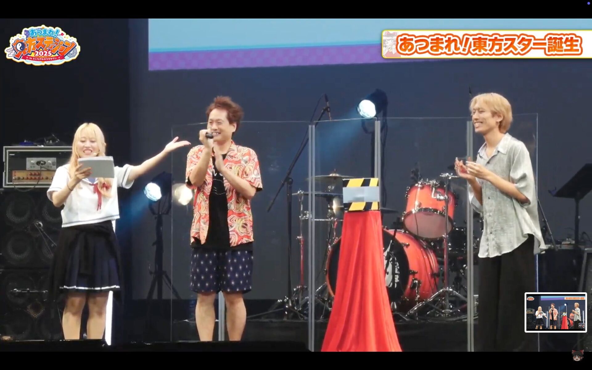 記事画像6: イベントで壇上に立つ3人の人物とドラムセット。