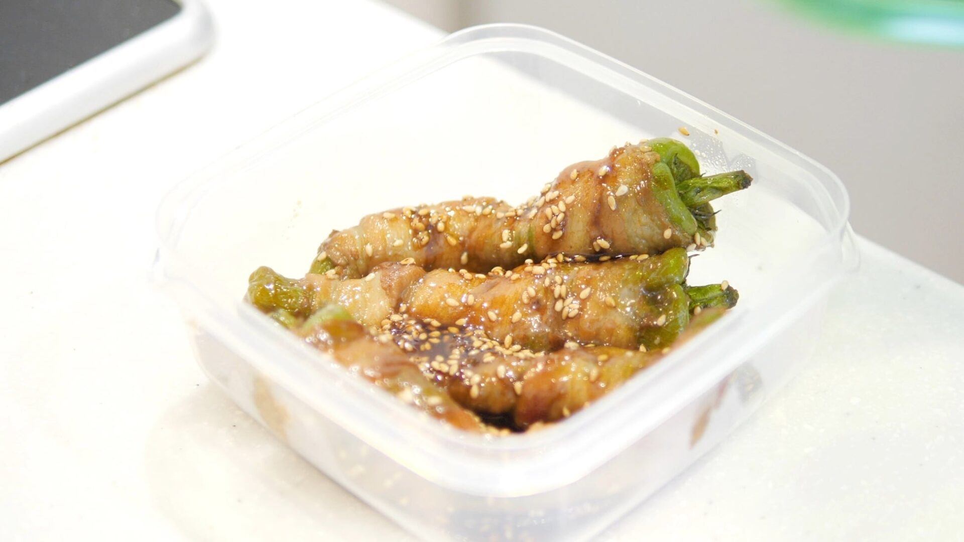 記事画像7: ピーマンの肉巻きがタレと胡麻で和えられ、容器に盛られている