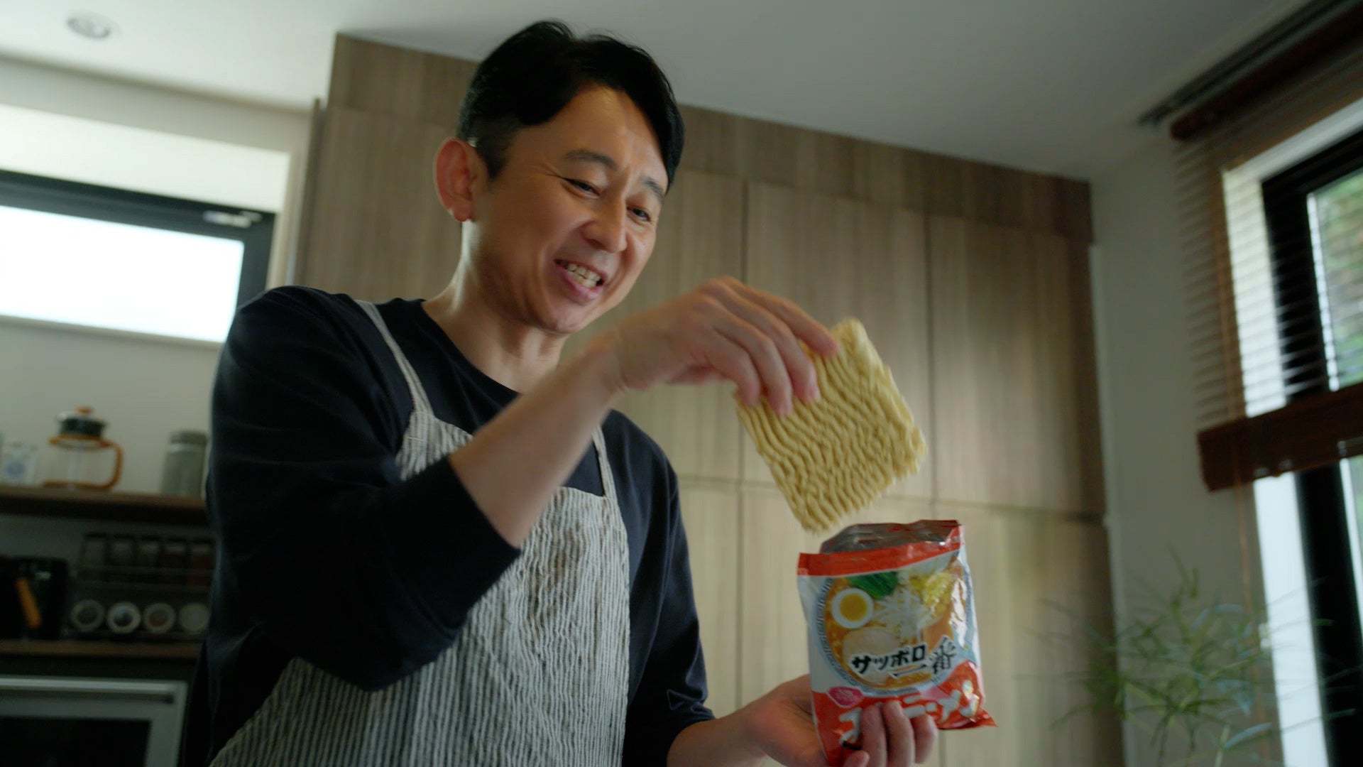 記事画像3: 男性がインスタントラーメンを取り出している様子。キッチンでの食事準備。
