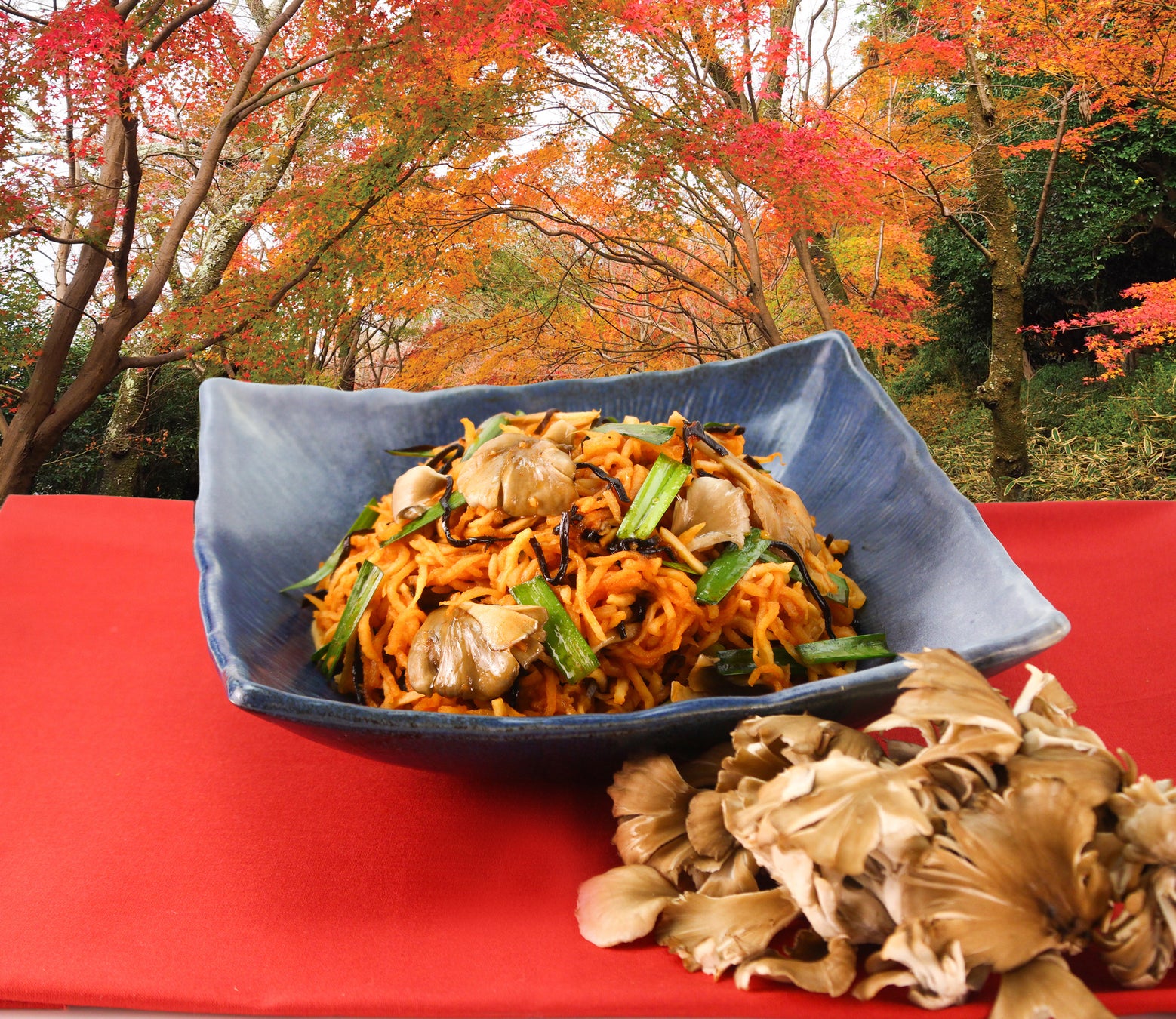 秋の紅葉を背景に、器に盛られたきのこの炒め物と舞茸