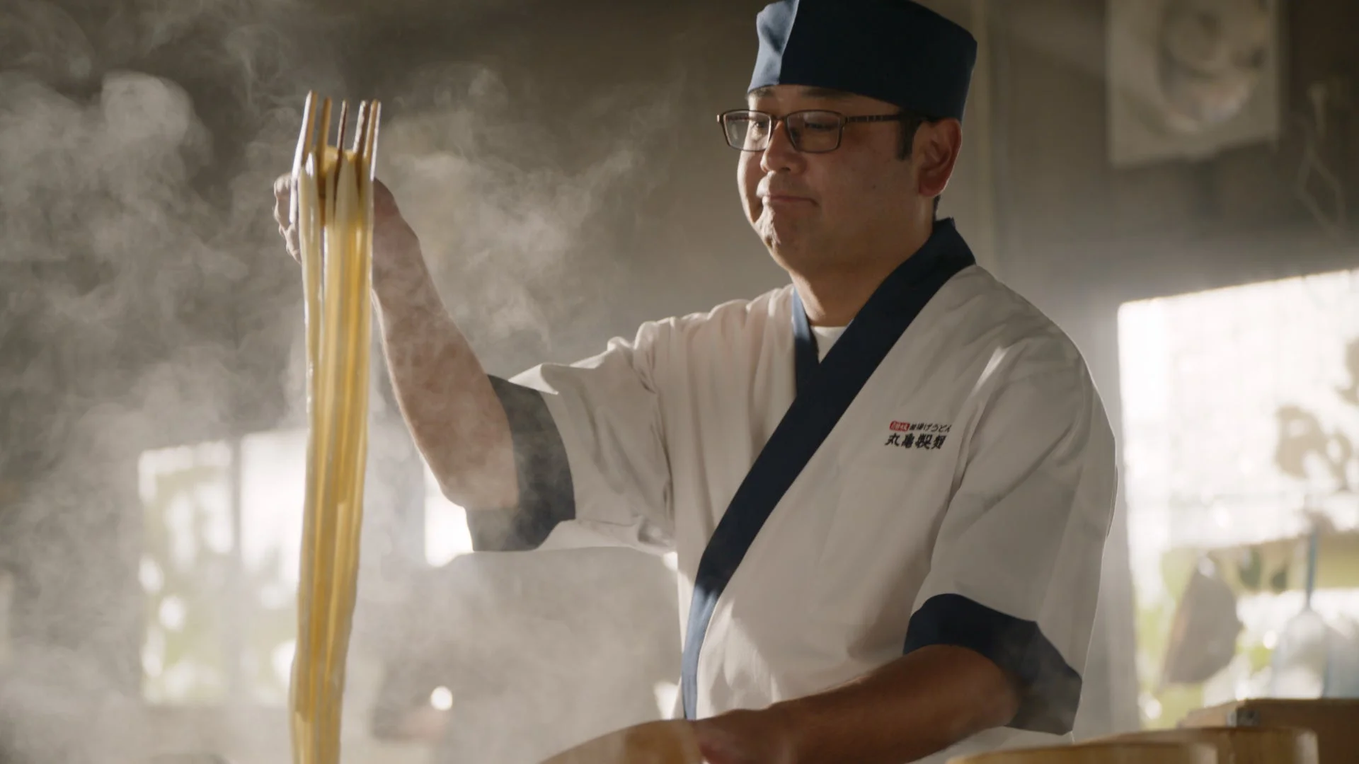 麺職人が茹でたてのうどんを湯気の中で持ち上げる様子