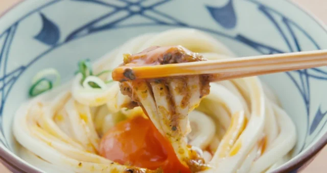 箸で持ち上げられたしび辛ラー油と卵黄のうどん