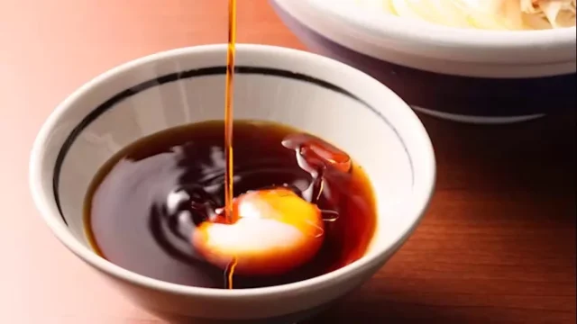 旨辛 豚つけ汁うどんのつけ汁に温泉玉子を落とす様子