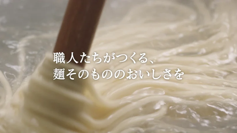 茹で釜の中でうどんをかき混ぜる様子と「職人たちがつくる、麺そのもののおいしさを」の文字