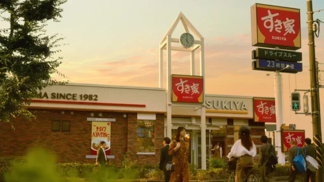 秋の夕暮れ時のすき家店舗外観と行き交う人々
