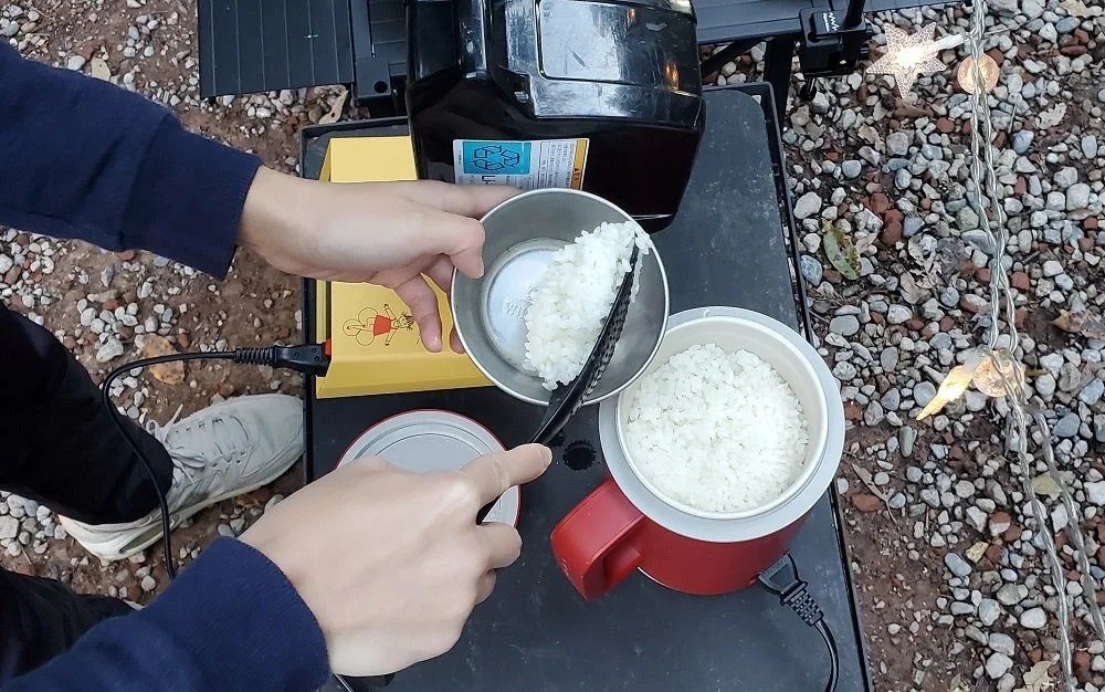 キャンプで炊き上がったご飯をミニ炊飯器から小皿によそう様子