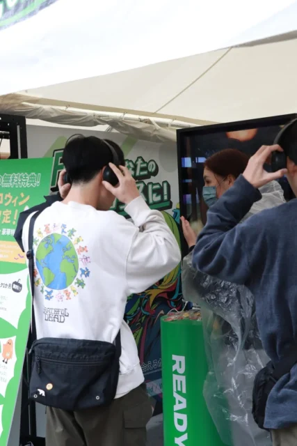 FLAIブースでヘッドホンを着用しAIとの会話を体験する来場者
