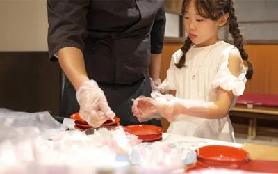 子供が寿司職人に教わりながら握り寿司体験をする様子