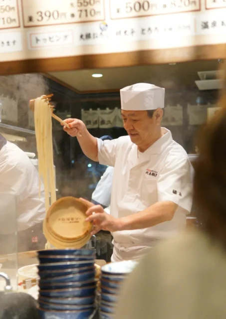 麺匠がうどんを茹で釜からすくい上げる様子