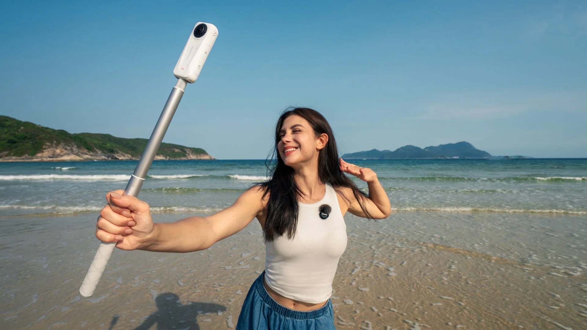 ビーチで見えない自撮り棒でInsta360 X4 Airを使って自撮りする女性