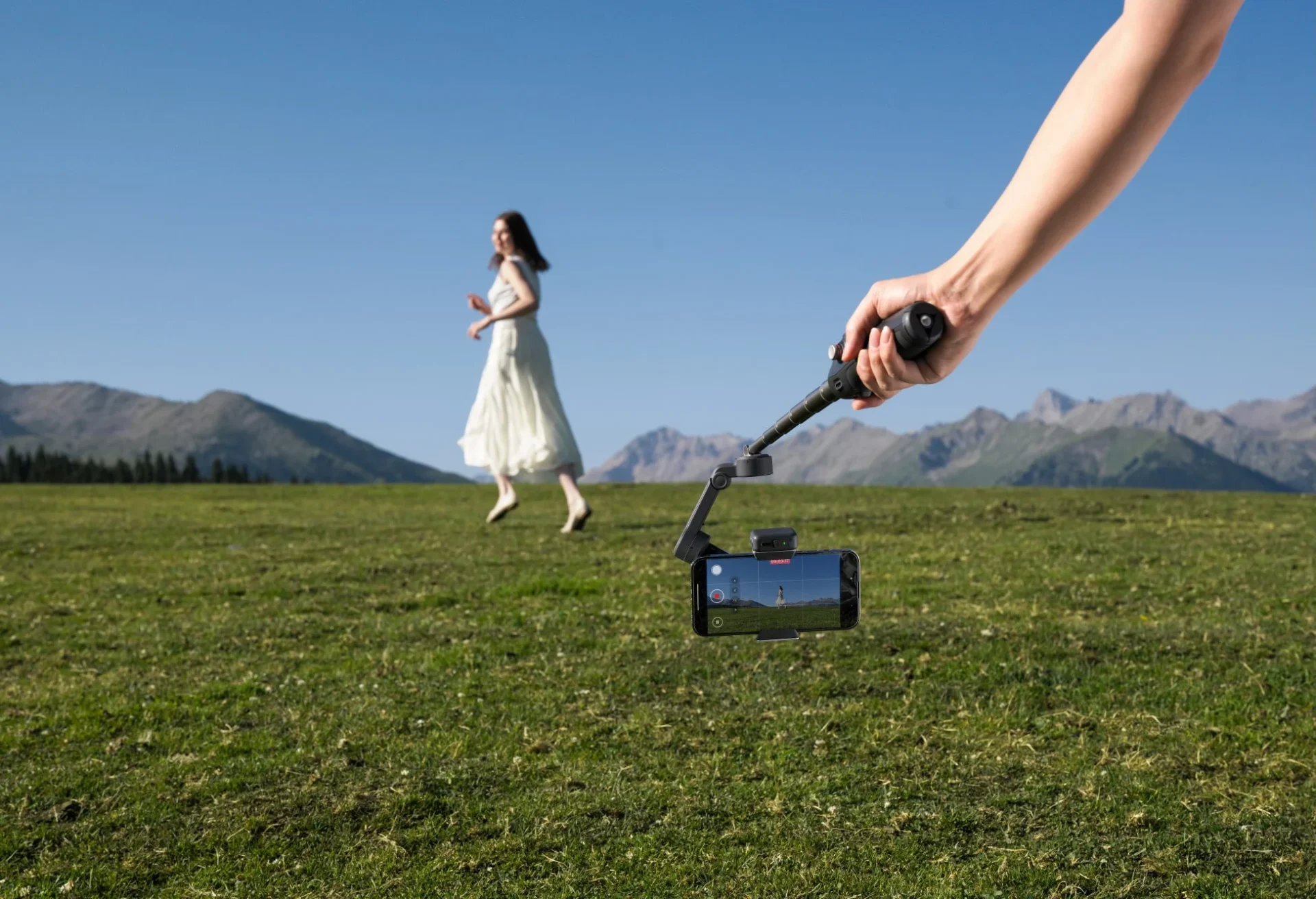 Osmo Mobile 8をローアングルで持ち、草原を歩く女性を撮影する様子