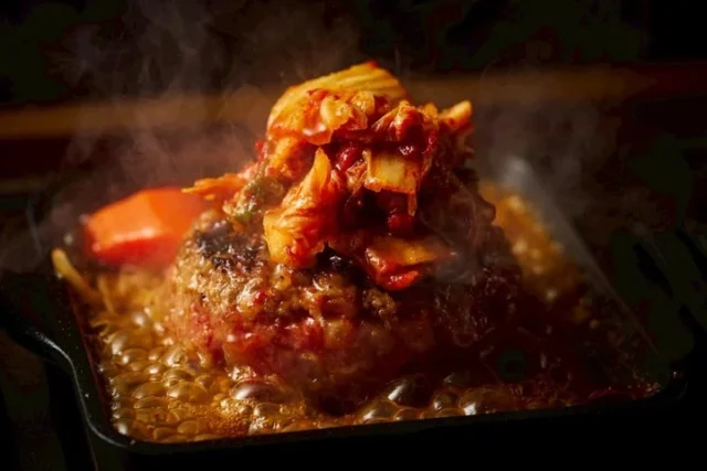 鉄板で焼かれるキムチトッピングのハンバーグ