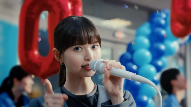 マイクを持って歌うソフトバンクショップクルー姿の齋藤飛鳥さん