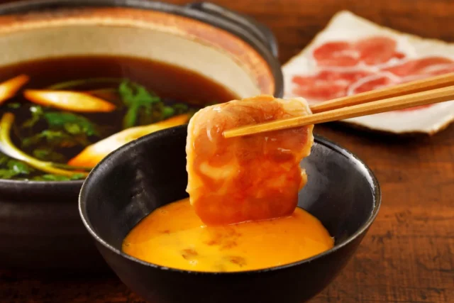 鴨肉を卵と黒煎り七味につけて食べる様子