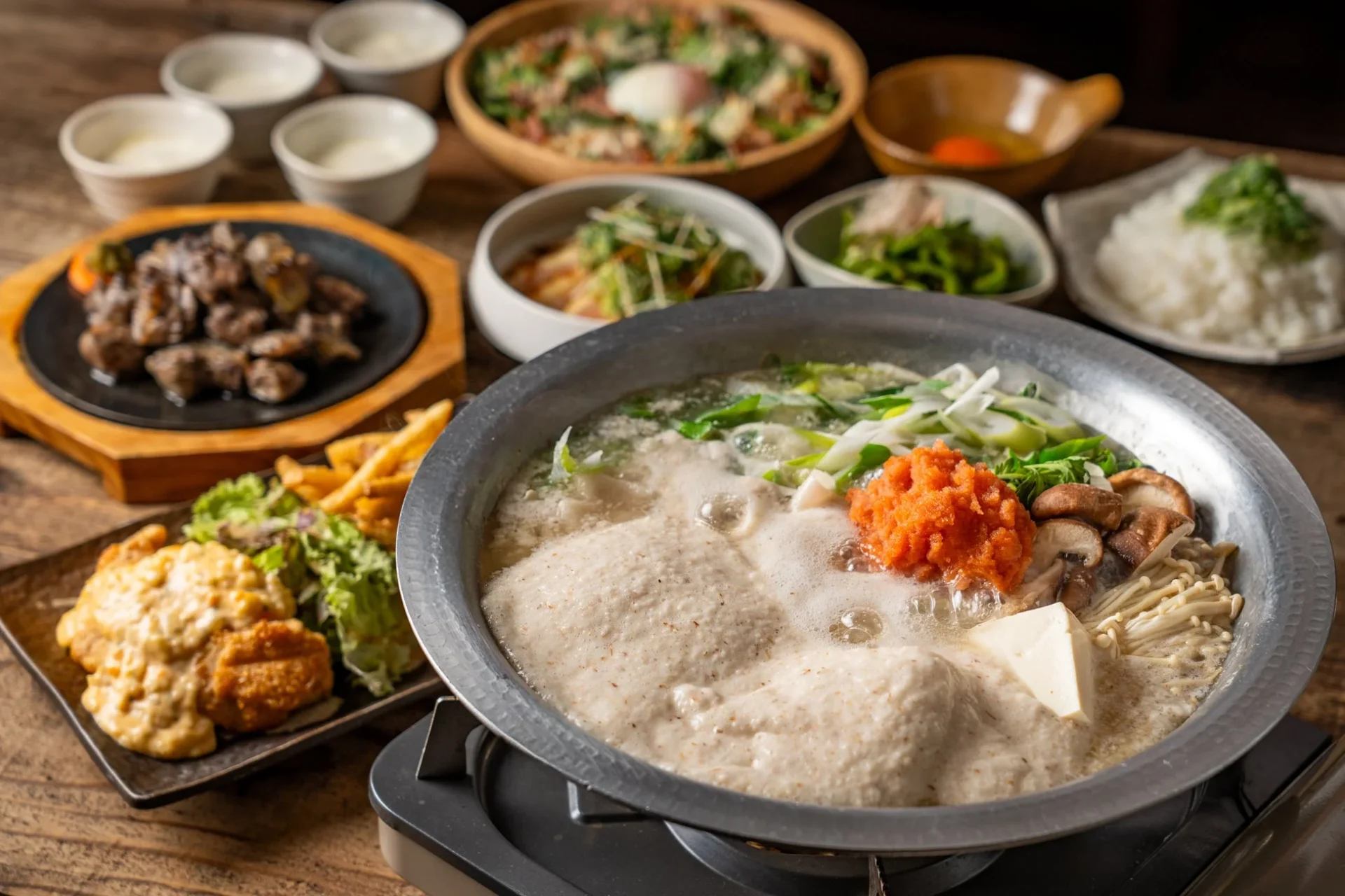 九州野菜の明太とろろ鍋満足コースの全景。明太とろろ鍋を中心に、地鶏炭火焼、チキン南蛮などの料理が並ぶ。