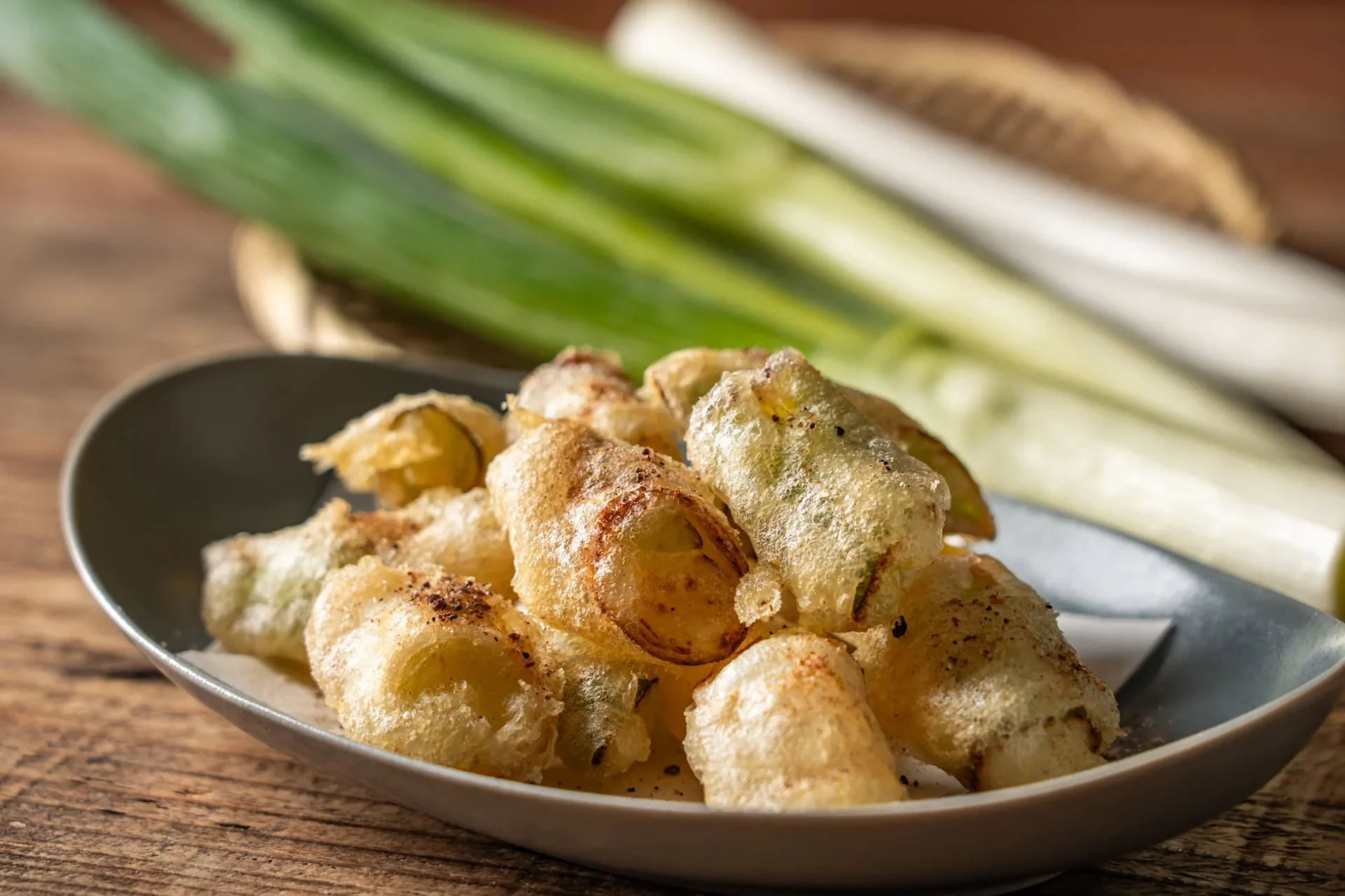 栗原ねぎのサクサクフリット。揚げられたねぎが皿に盛り付けられ、奥には生ねぎが見える。