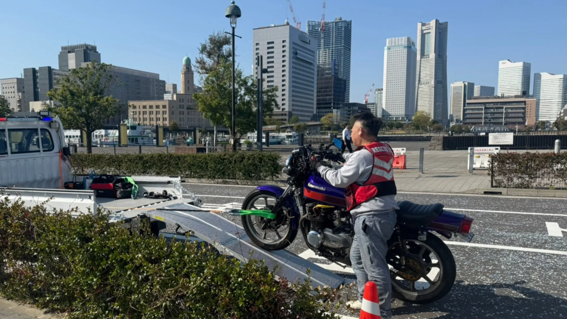 横浜の街並みを背景にバイクをレッカー車に積み込む作業員
