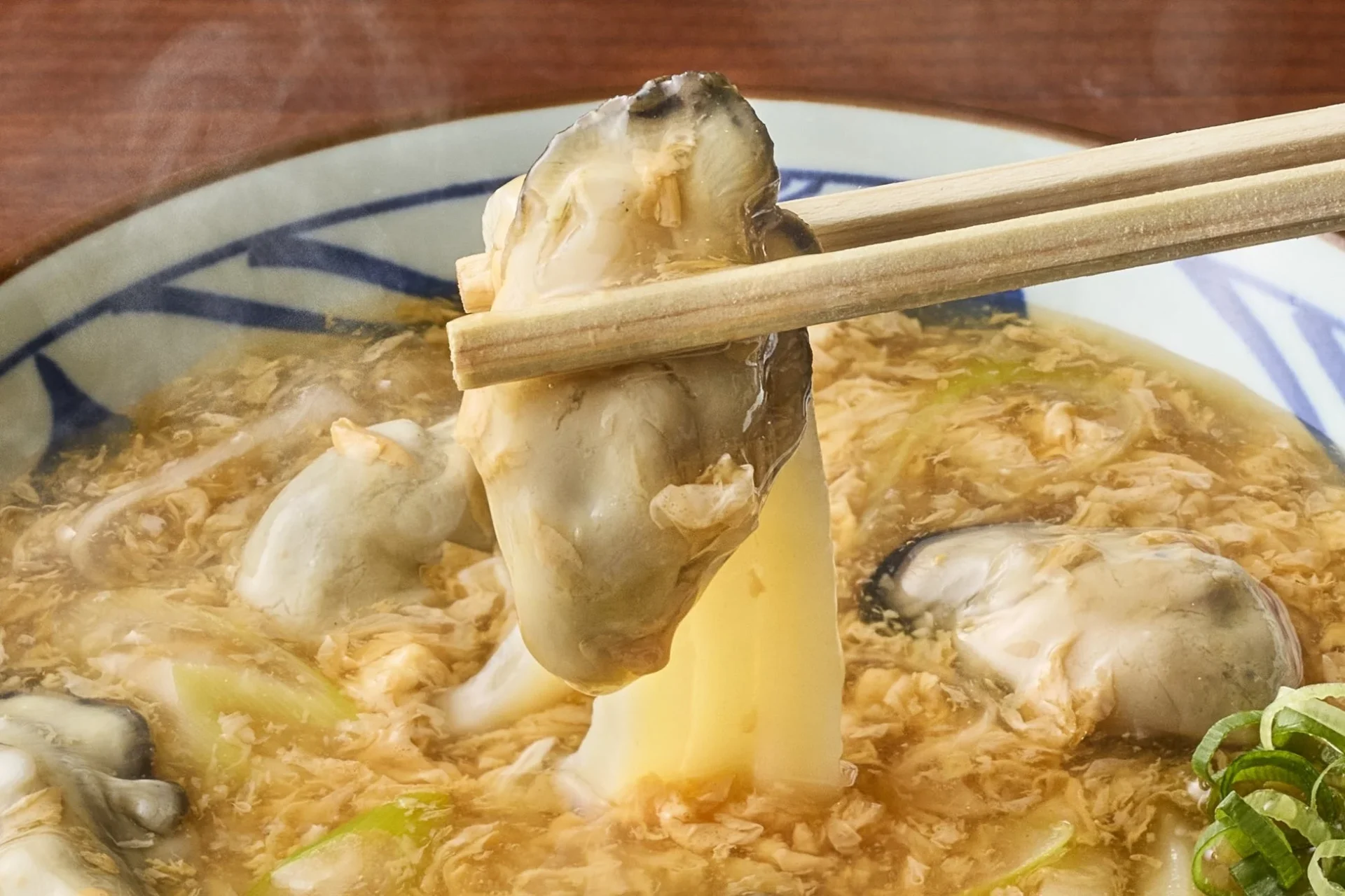 丸亀製麺の牡蠣たまあんかけうどん、ぷりぷりの牡蠣が箸で持ち上げられた様子