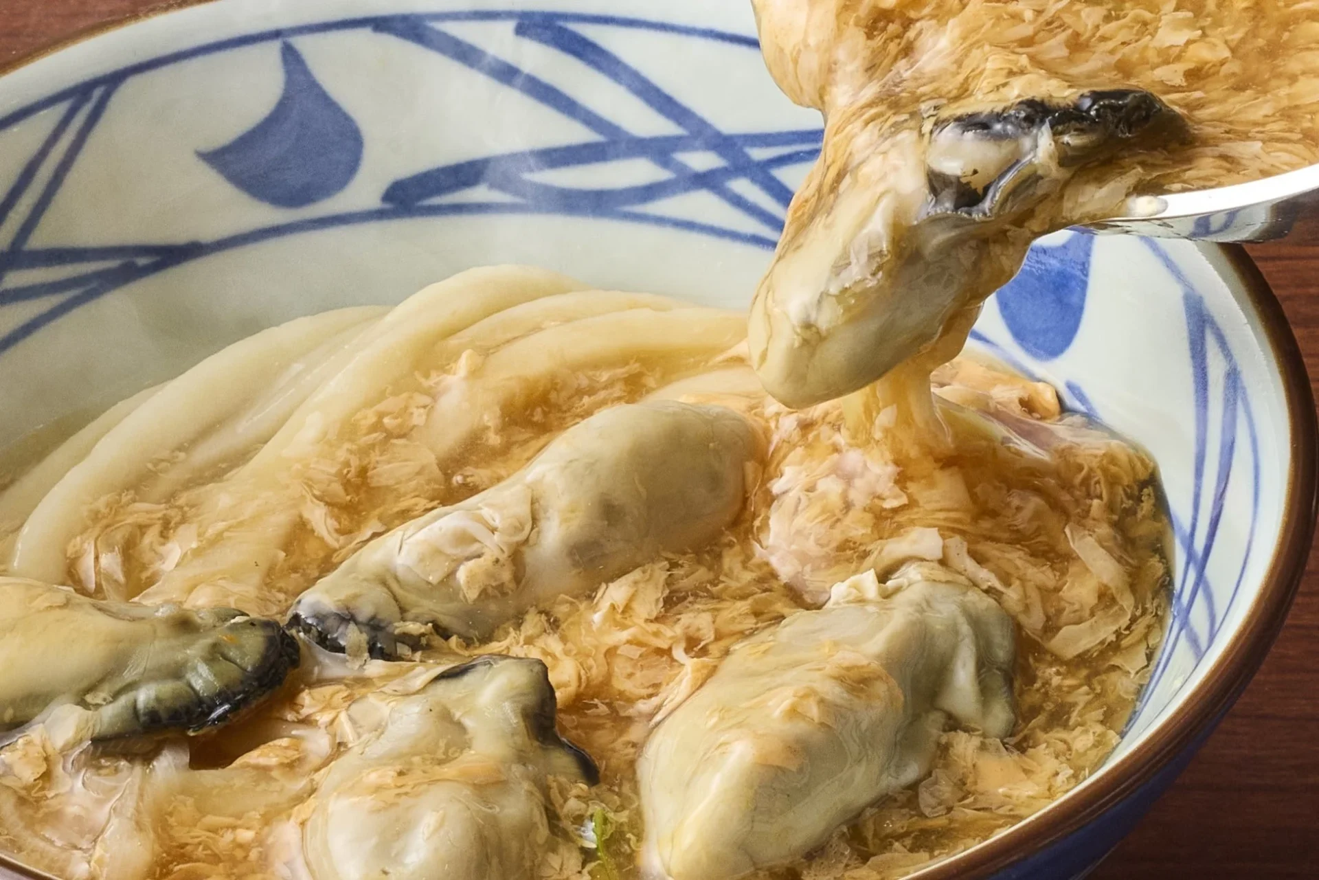 丸亀製麺の牡蠣たまあんかけうどん、お店で手仕込みされた玉子あんかけを注ぐ様子