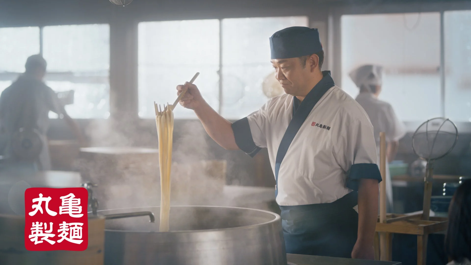丸亀製麺の麺職人が打ち立てのうどんを湯切りする様子