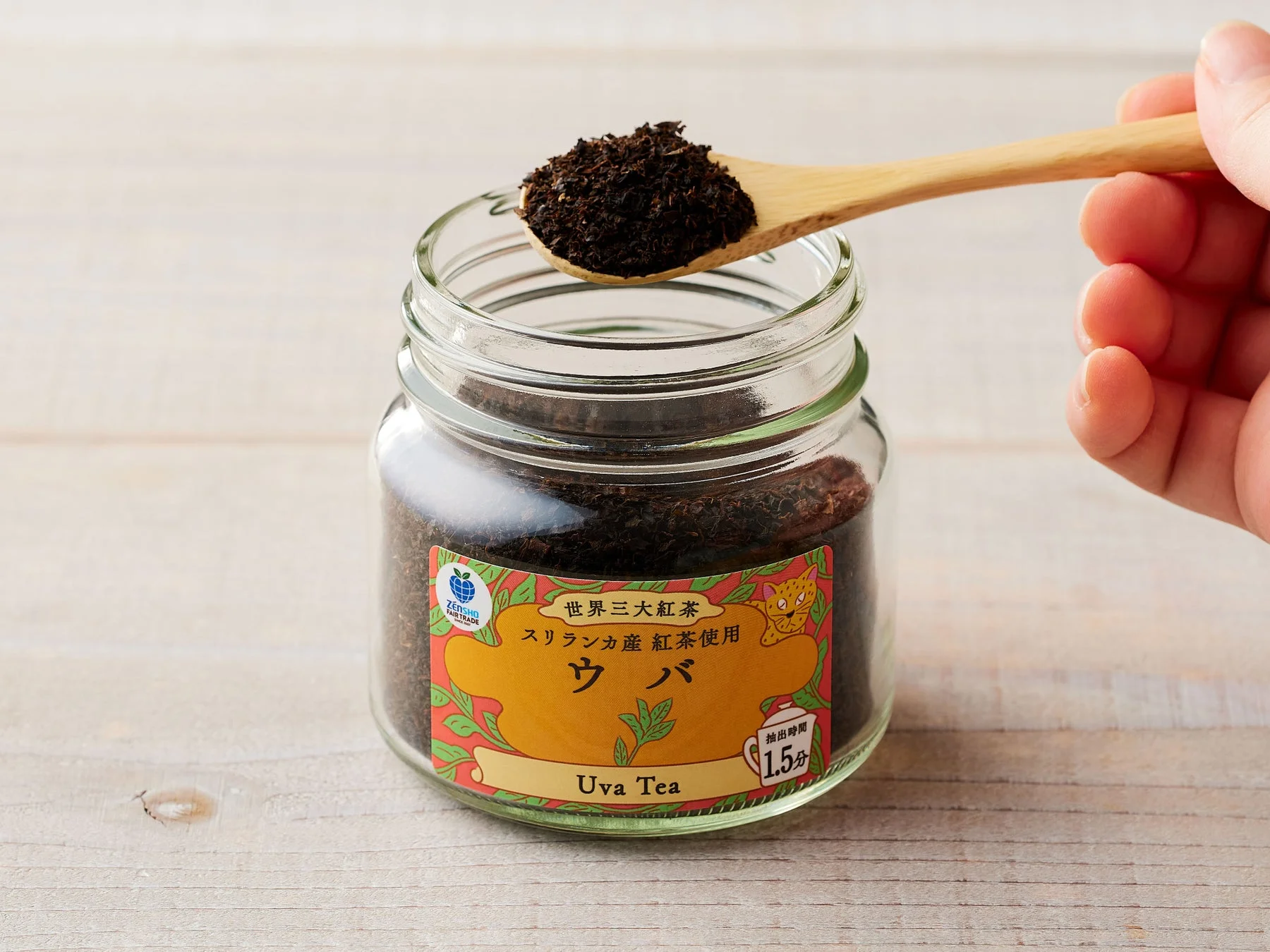 スプーンで掬われたウバ茶葉が入った瓶。世界三大紅茶の表示とフェアトレードロゴがある