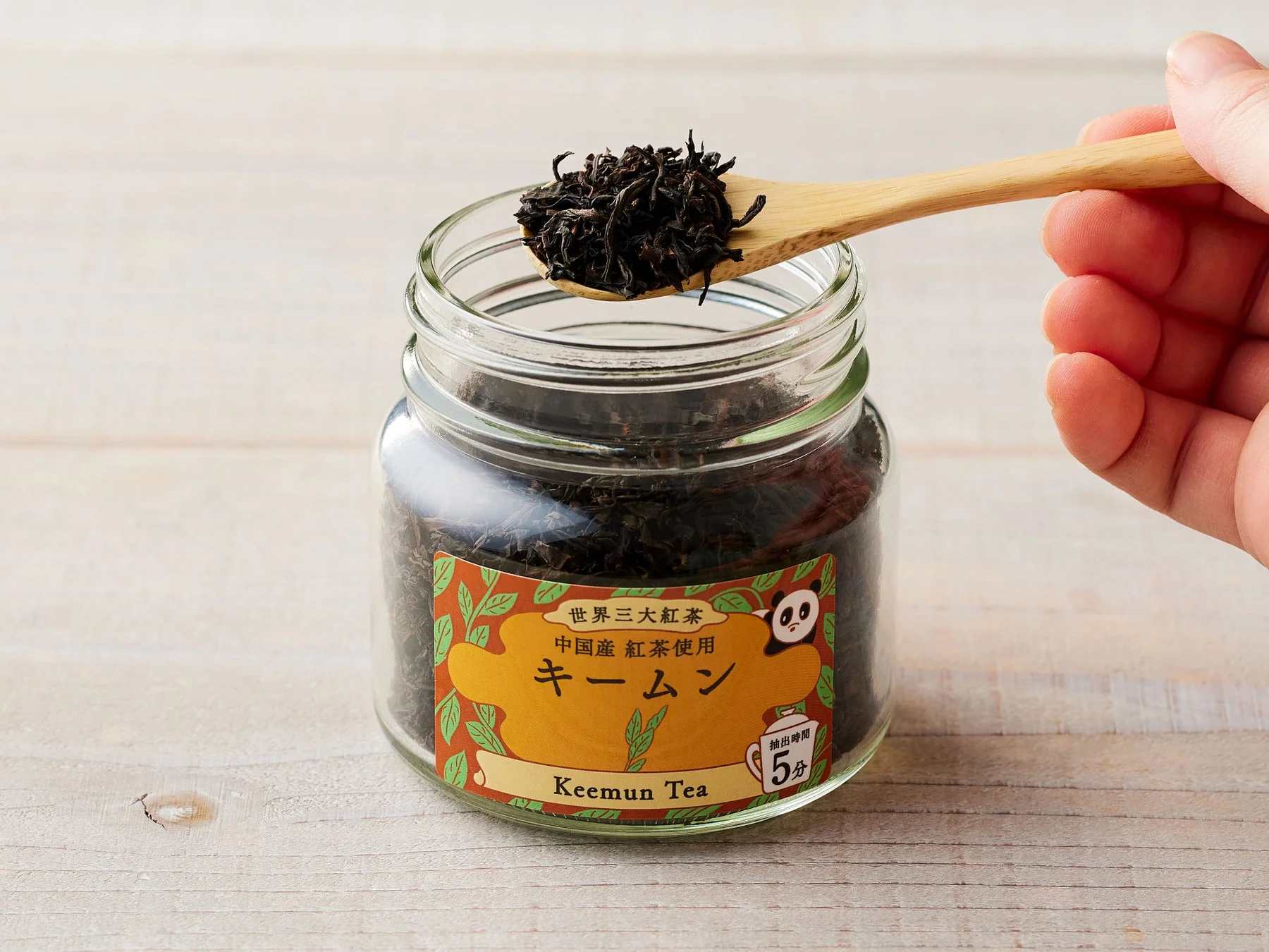 スプーンで掬われたキームン茶葉が入った瓶。世界三大紅茶の表示とパンダのイラストがある