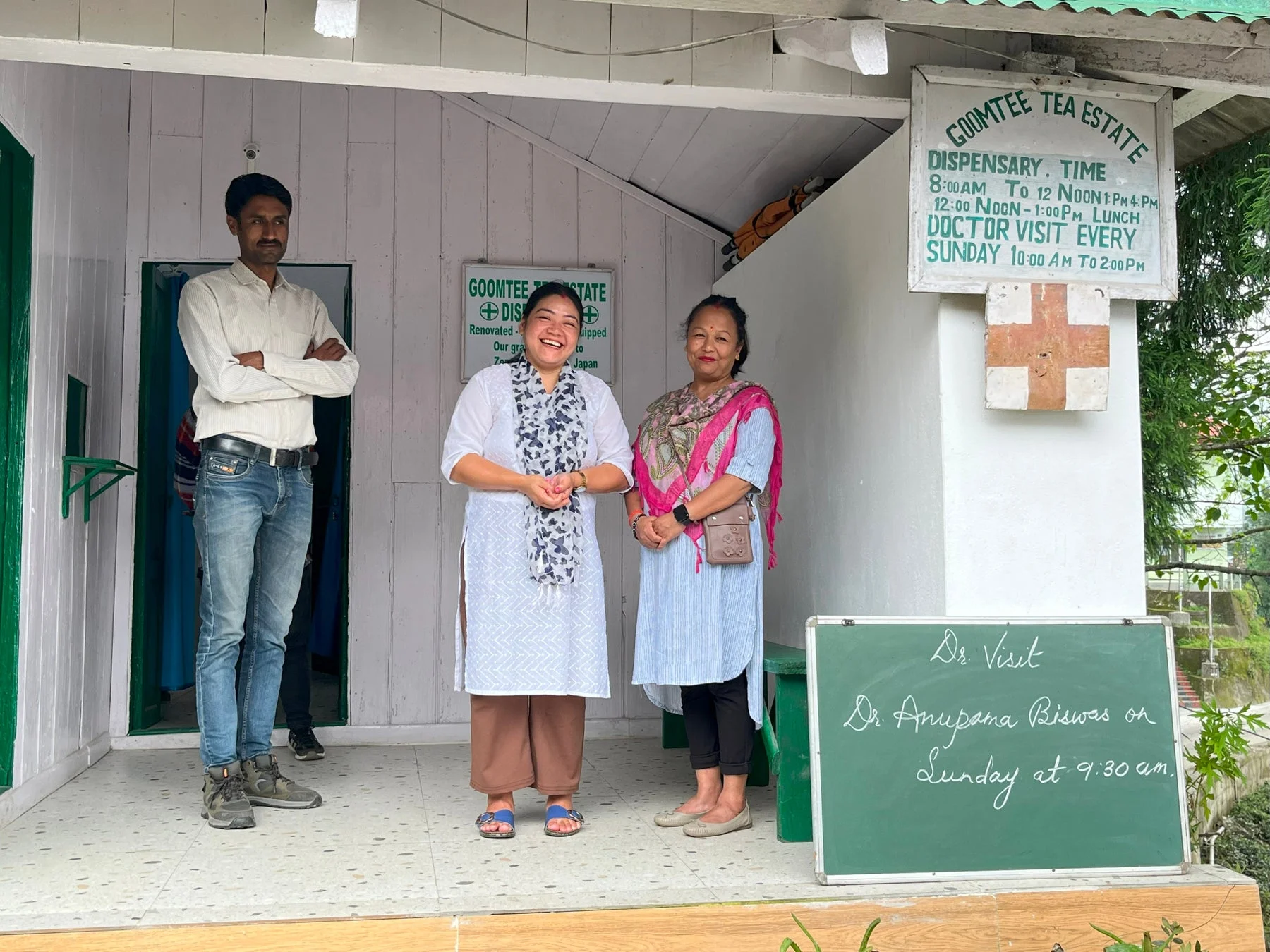 インドの診療所の入り口で笑顔で立つ人々。診療時間を示す看板が見える