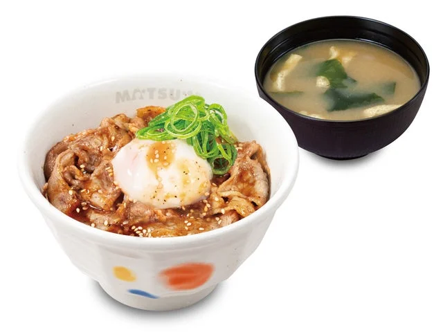松屋の「新焼き牛めし」のアップ写真。半熟卵と青ネギがトッピングされている。