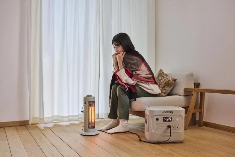 Jackeryポータブル電源でヒーターを使用し暖をとる女性。