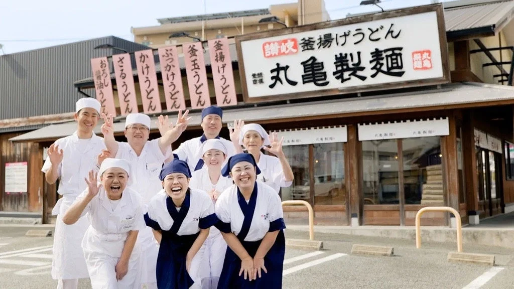 丸亀製麺の店舗前で笑顔を見せる従業員たち