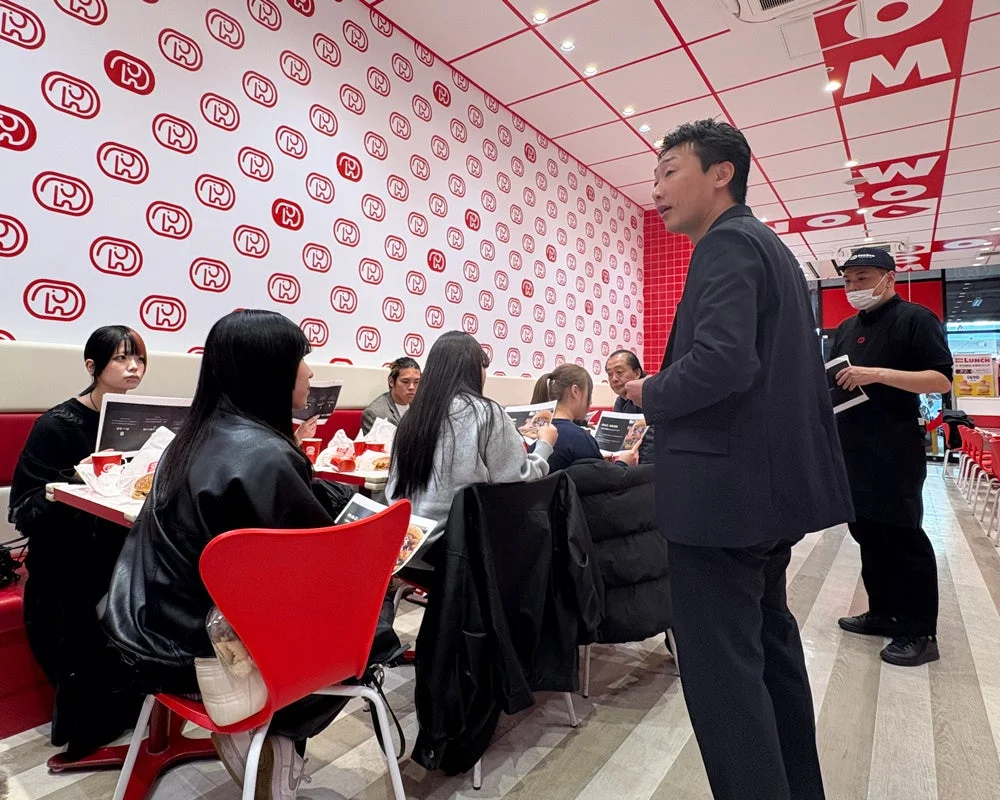 ドムドムハンバーガー赤羽店で新メニューについて話し合う学生と社員