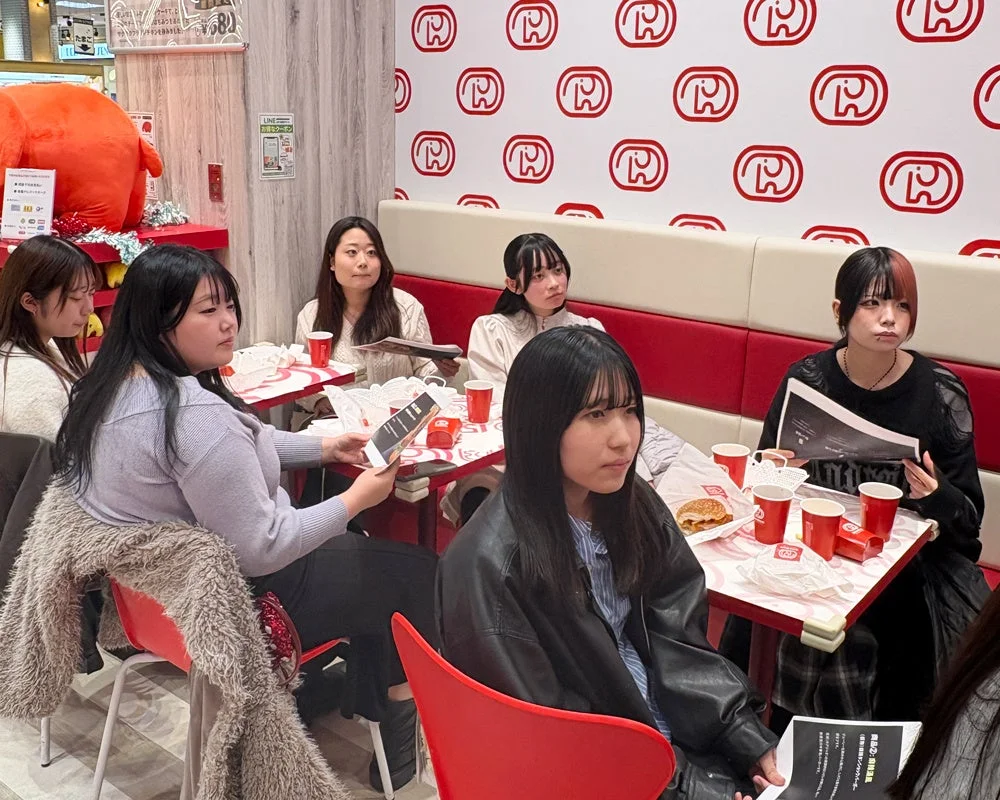 ドムドムハンバーガーの新メニュー試食会で説明を聞く学生たち