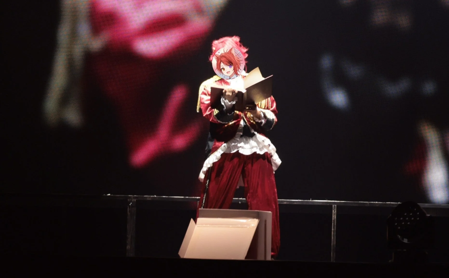 ライブで赤い衣装をまとい本を読むようなポーズをとる莉犬