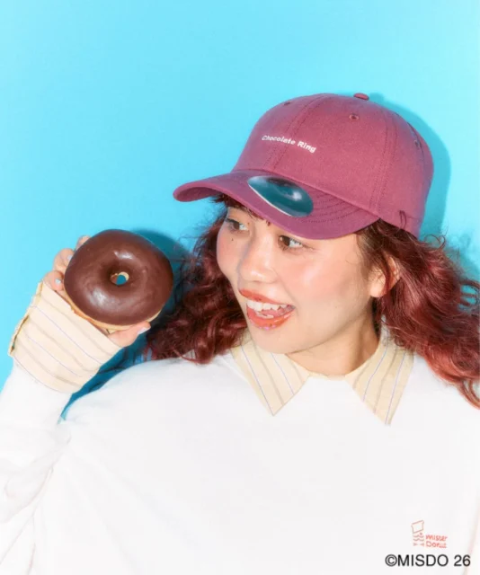 チョコレートリングの刺繍入りキャップを着用しドーナツを持つモデル