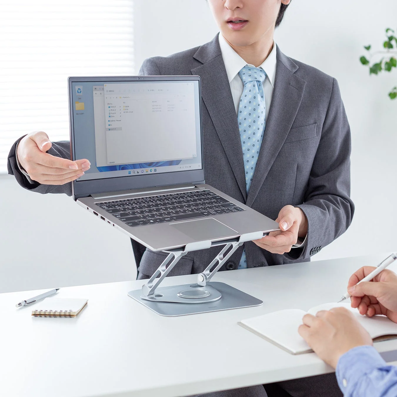 ノートパソコンスタンドに載せたPCの画面を会議で共有するビジネスパーソン