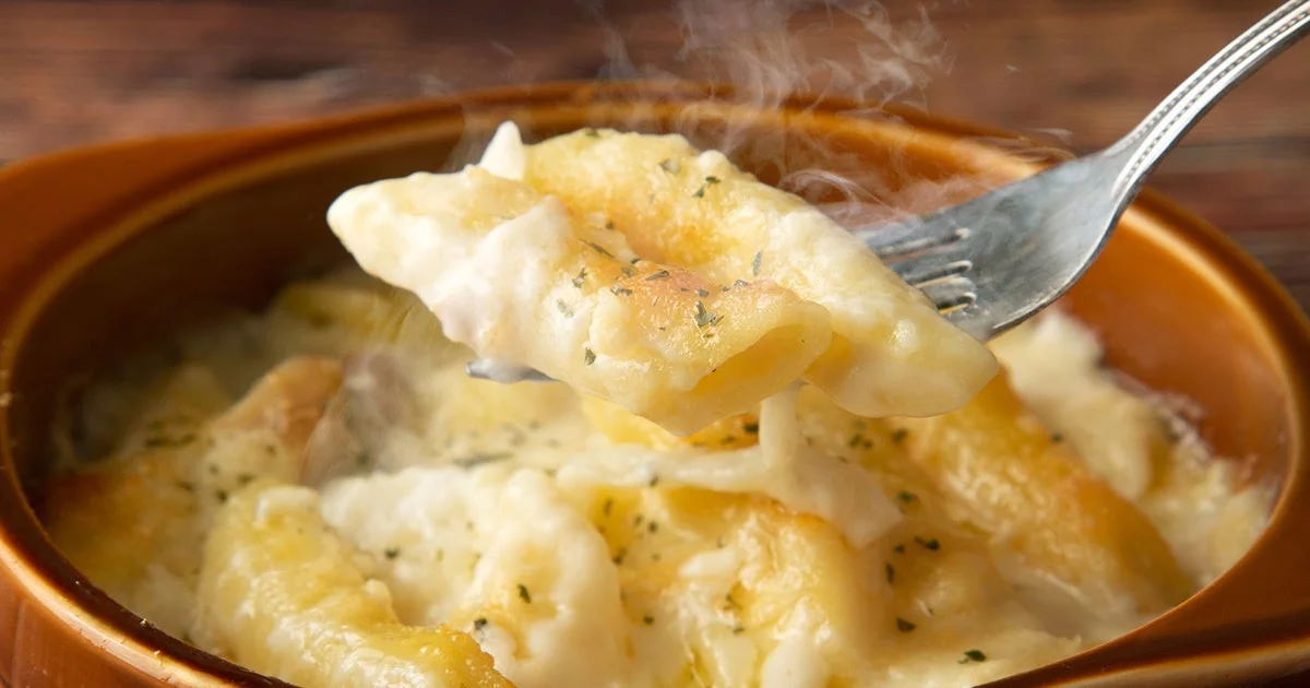 アツアツのグラタン皿に入ったペンネグラタンをフォークですくっている様子。湯気が立ち上り、濃厚なソースが絡んでいる。