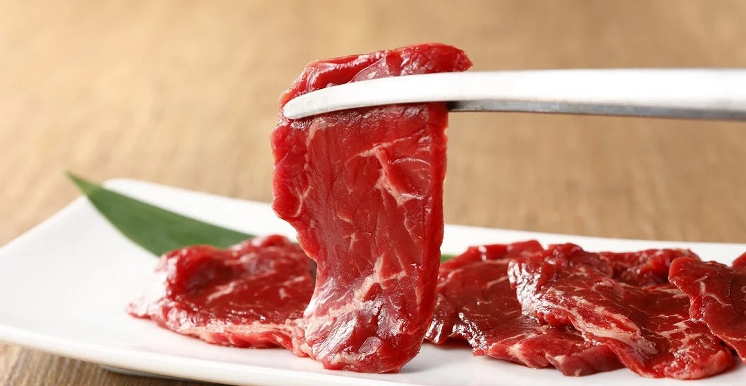 トングで持ち上げられた新鮮な「ワタミカルビ」のアップ、皿には複数の肉が盛られている