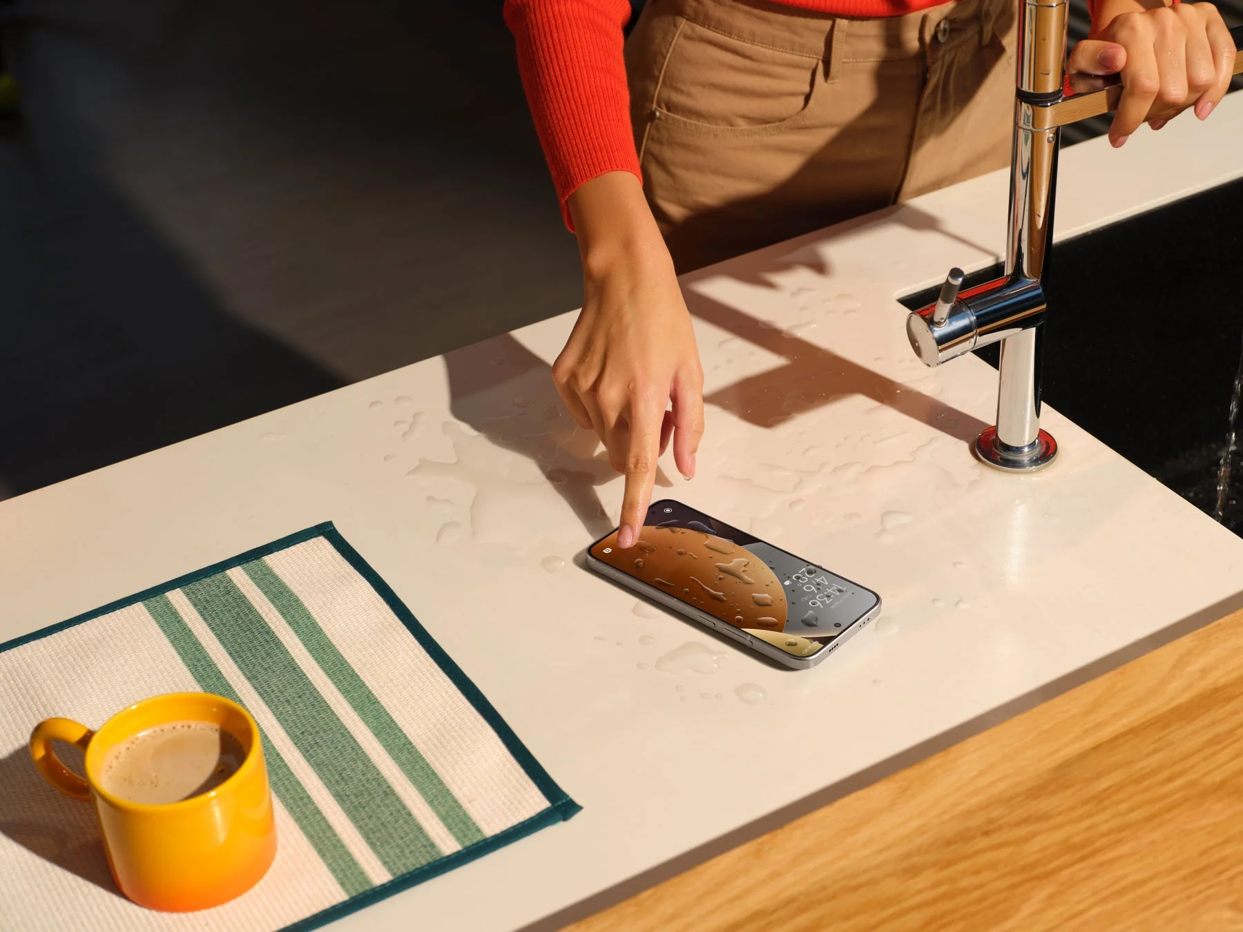 キッチンで水滴がかかったREDMI Note 15 Pro 5Gを操作する手、高い防水性能を示す