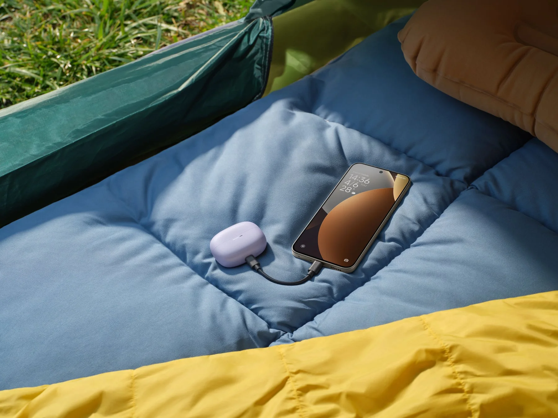 寝袋の上でワイヤレスイヤホンを充電するREDMI Note 15 Pro 5G、大容量バッテリーを示す