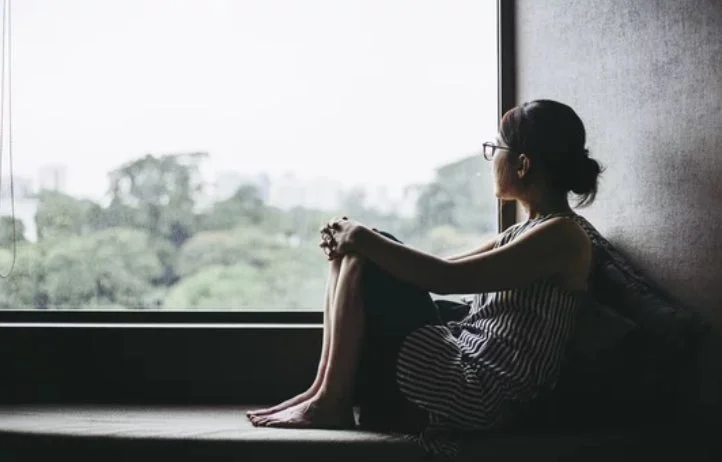 窓の外を眺める女性のシルエット。現代人の不安や孤独を表現。