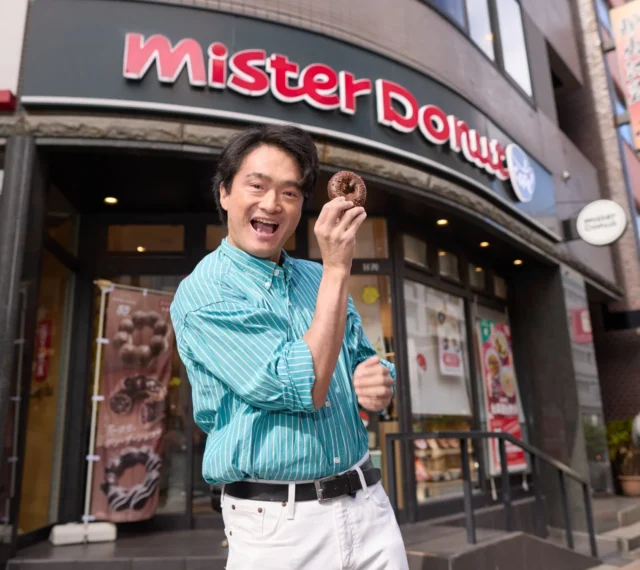 ミスタードーナツの店舗前でドーナツを持つ奥村泰人さん